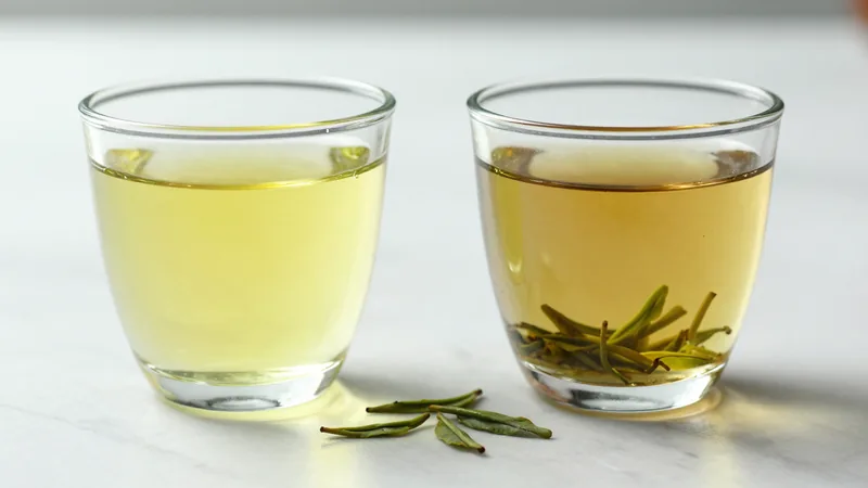 Two clear glass cups of green tea side by side on a white counter, one bright clear yellow-green and one darker and slightly cloudy