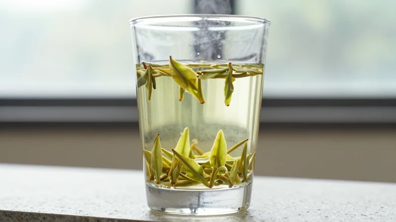 Flat, sword-shaped pale green Longjing leaves standing and sinking in a clear glass of hot water