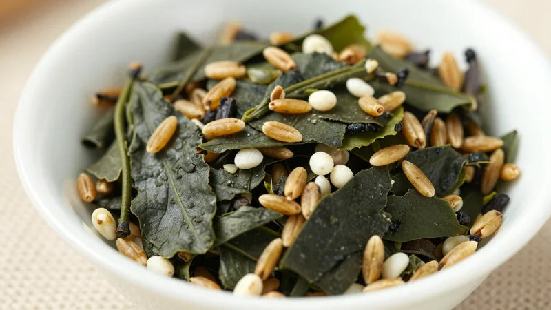 Close-up of genmaicha in a white ceramic dish: flat green tea leaves mixed with golden toasted rice grains and a few white popped kernels